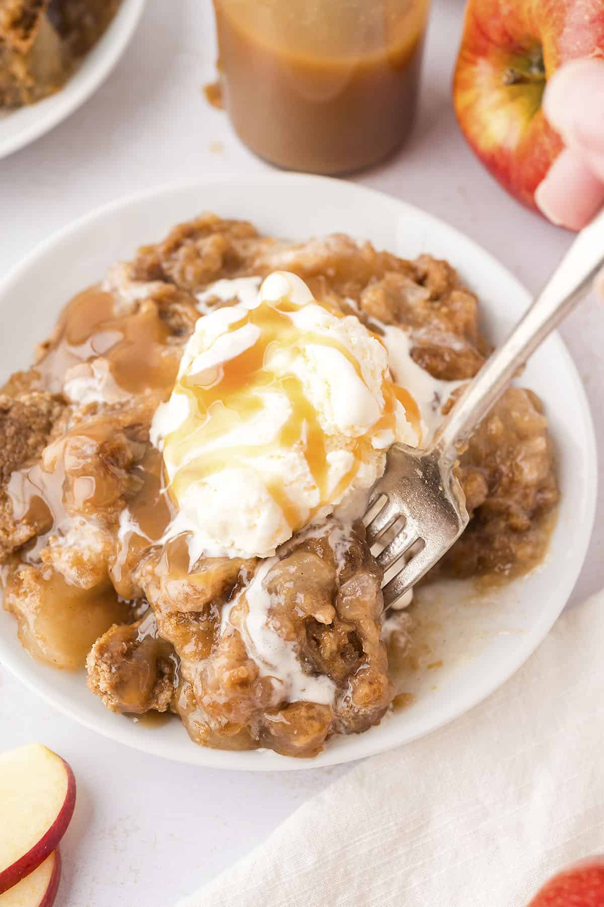 Fork taking a scoop of caramel apple dump cake from small white plate.