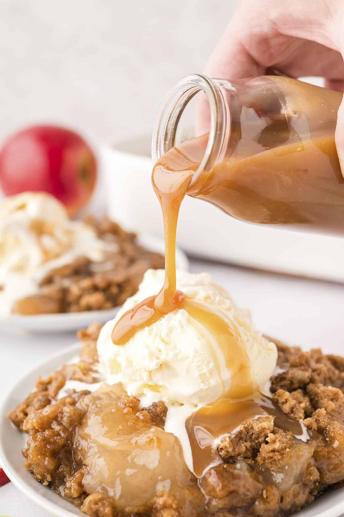 Caramel sauce being drizzled over caramel apple dump cake and vanilla ice cream.