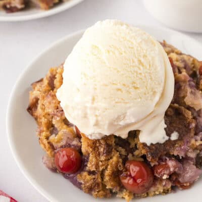 Cherry pineapple dump cake on white plate topped with ice cream.