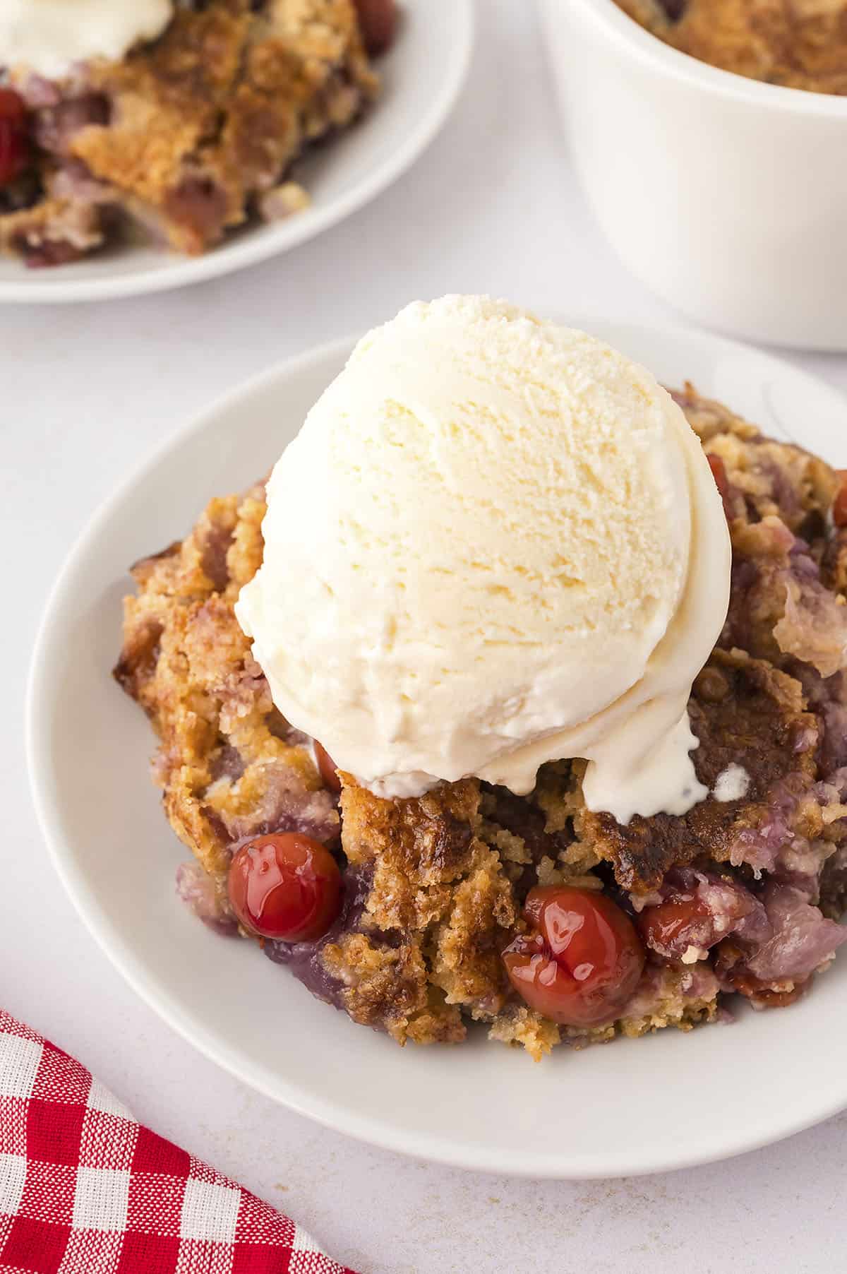 Cherry pineapple dump cake on white plate topped with ice cream.