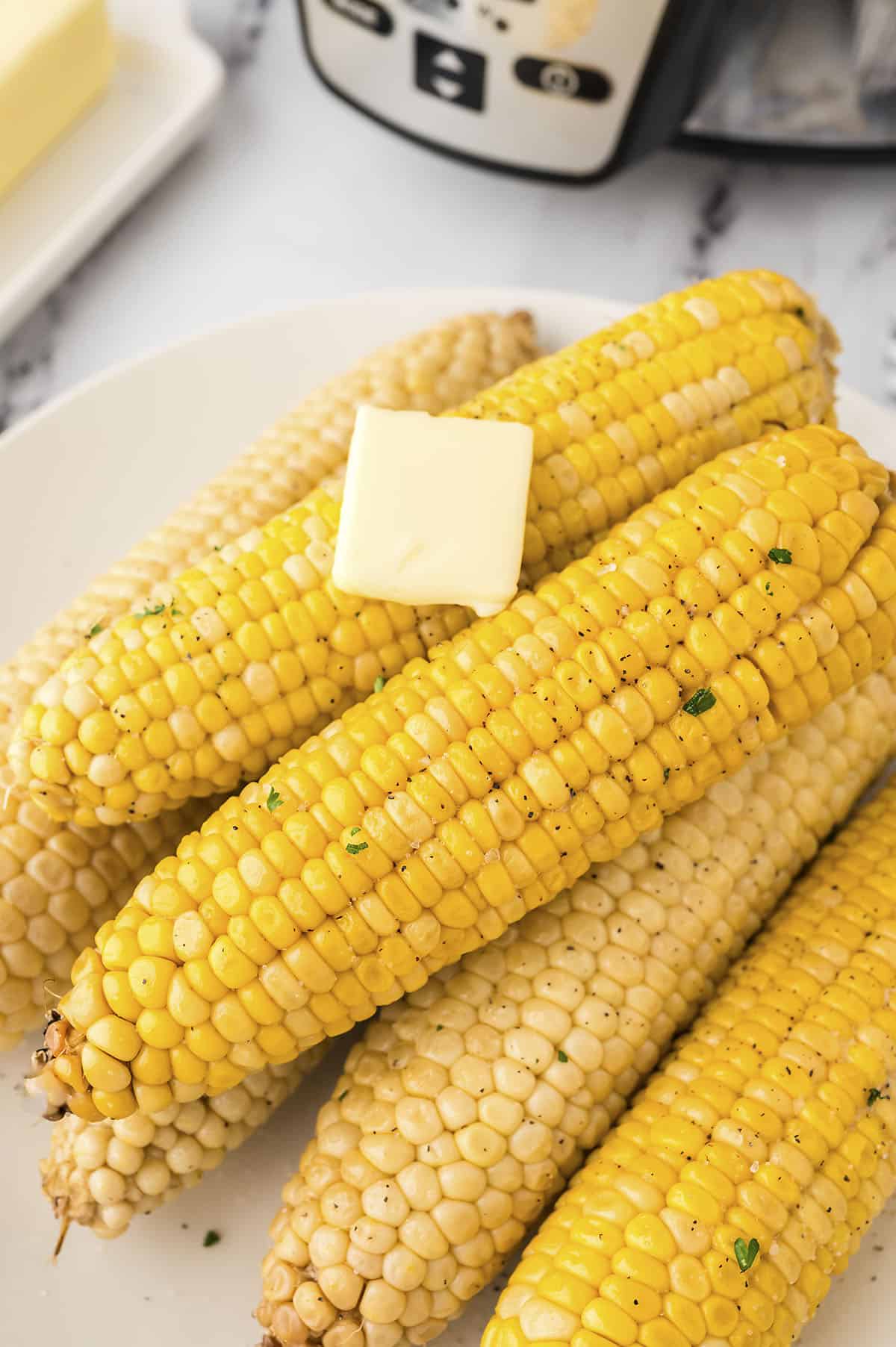 Slow cooker corn on the cob piled on platter with pat of butter.