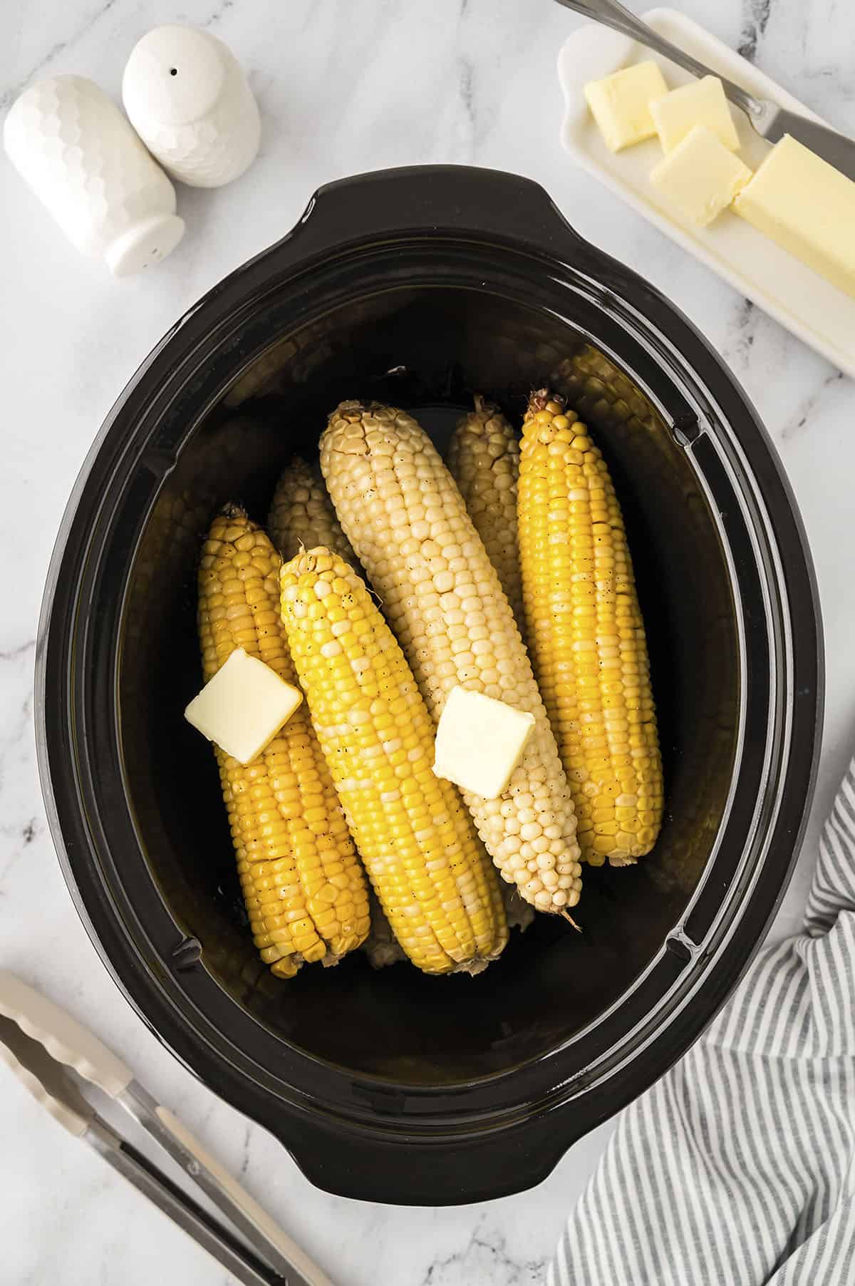 Corn on the cob in a crockpot topped with butter.