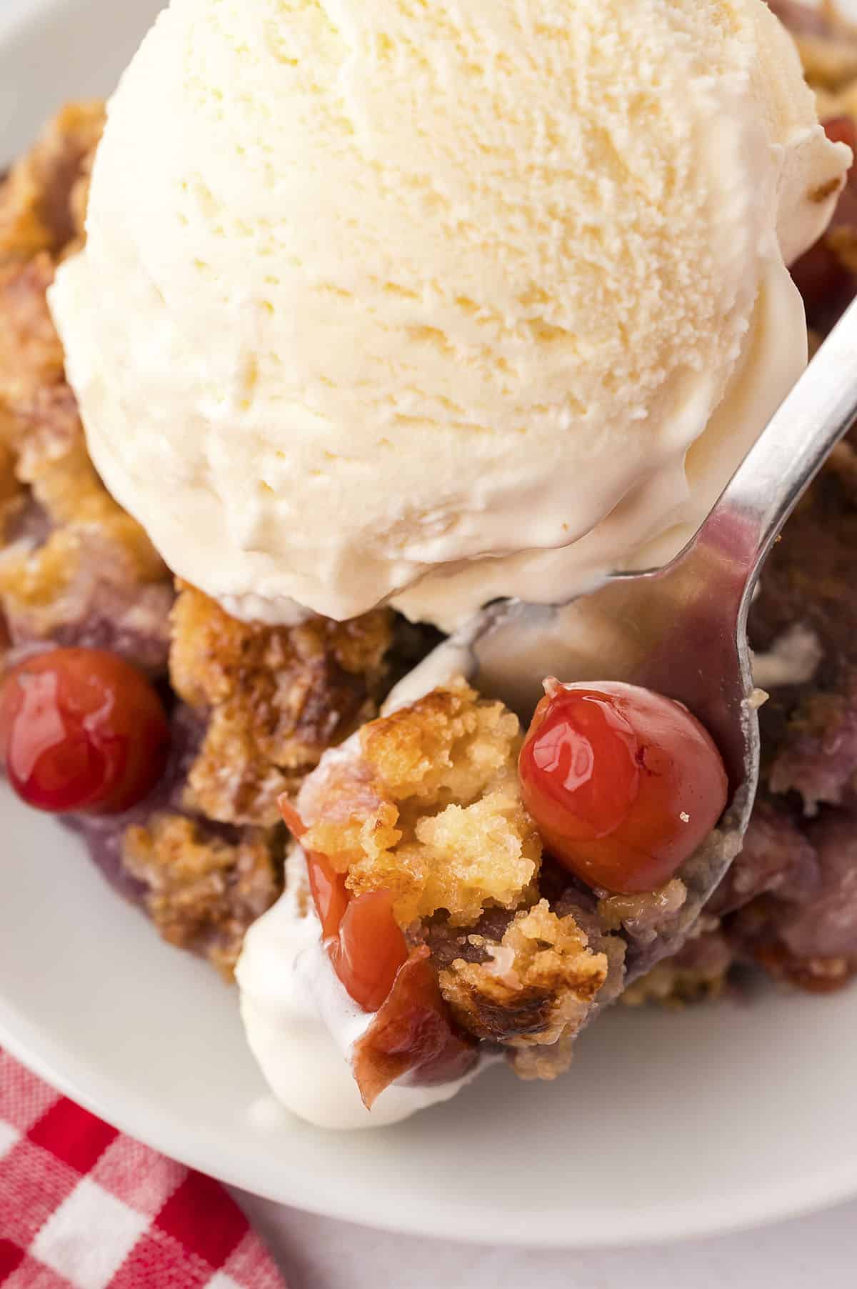 Vanilla ice cream and cherry pineapple dump cake on a spoon over a plate.