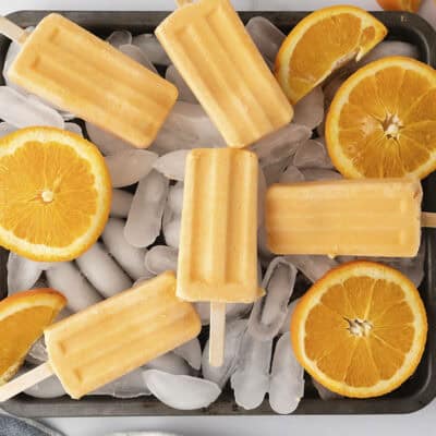 Orange cream popsicles piled on tray of ice.