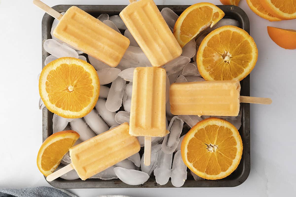 Orange cream popsicles piled on tray of ice.