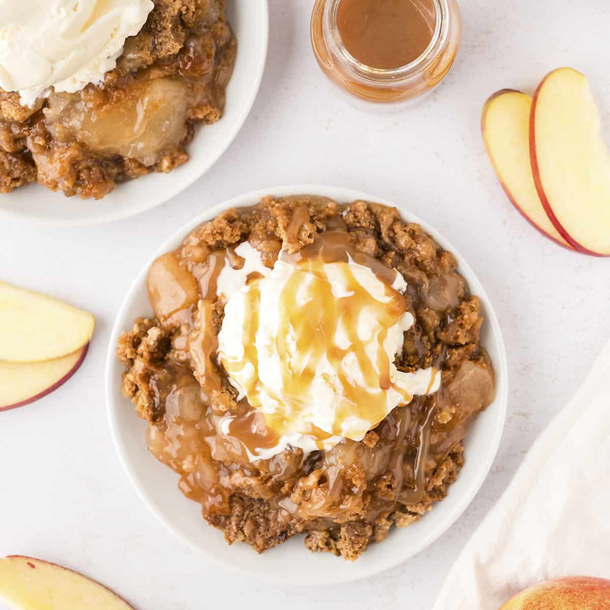 Caramel apple dump cake on white plate topped with a scoop of vanilla ice cream.