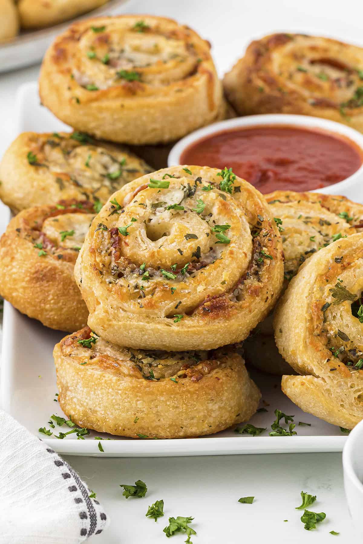 Stack of pizza pinwheels on plate with dish of pizza sauce.