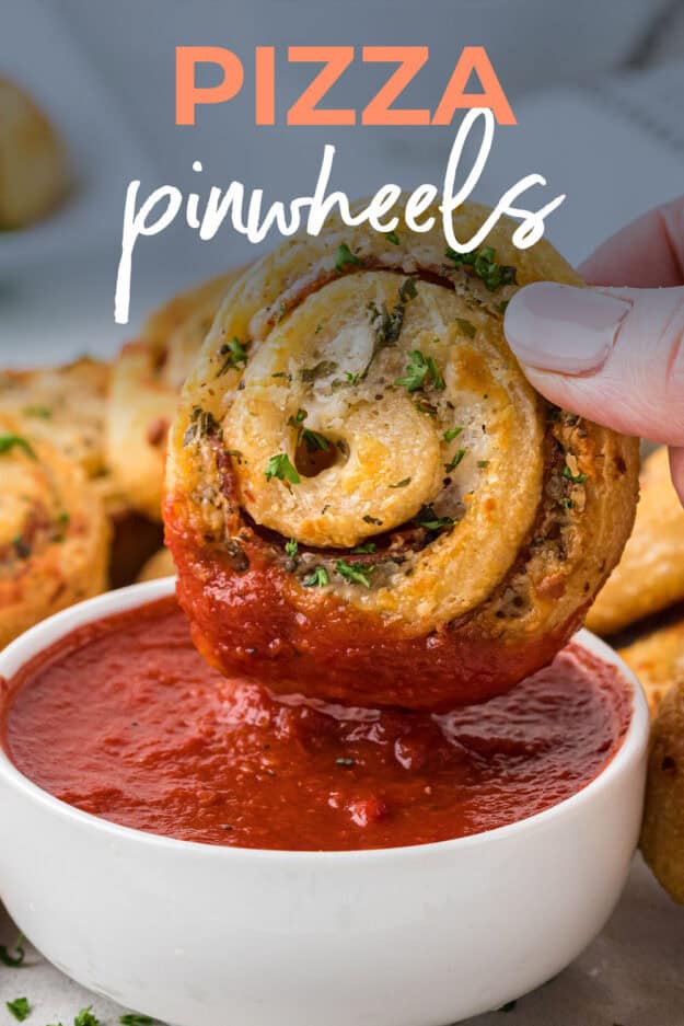 Hand dipping a pizza pinwheel into pizza sauce.