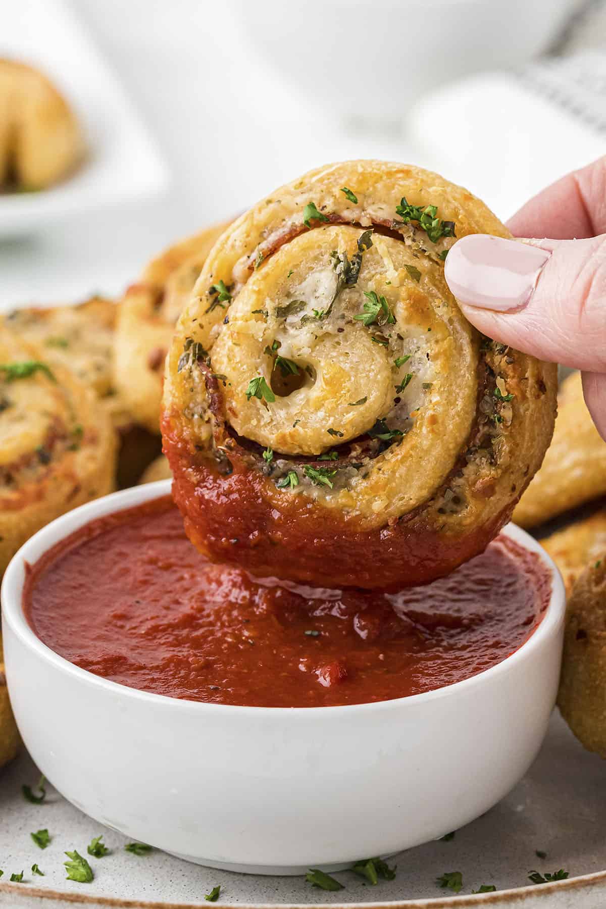 Hand dipping a pizza pinwheel into pizza sauce.