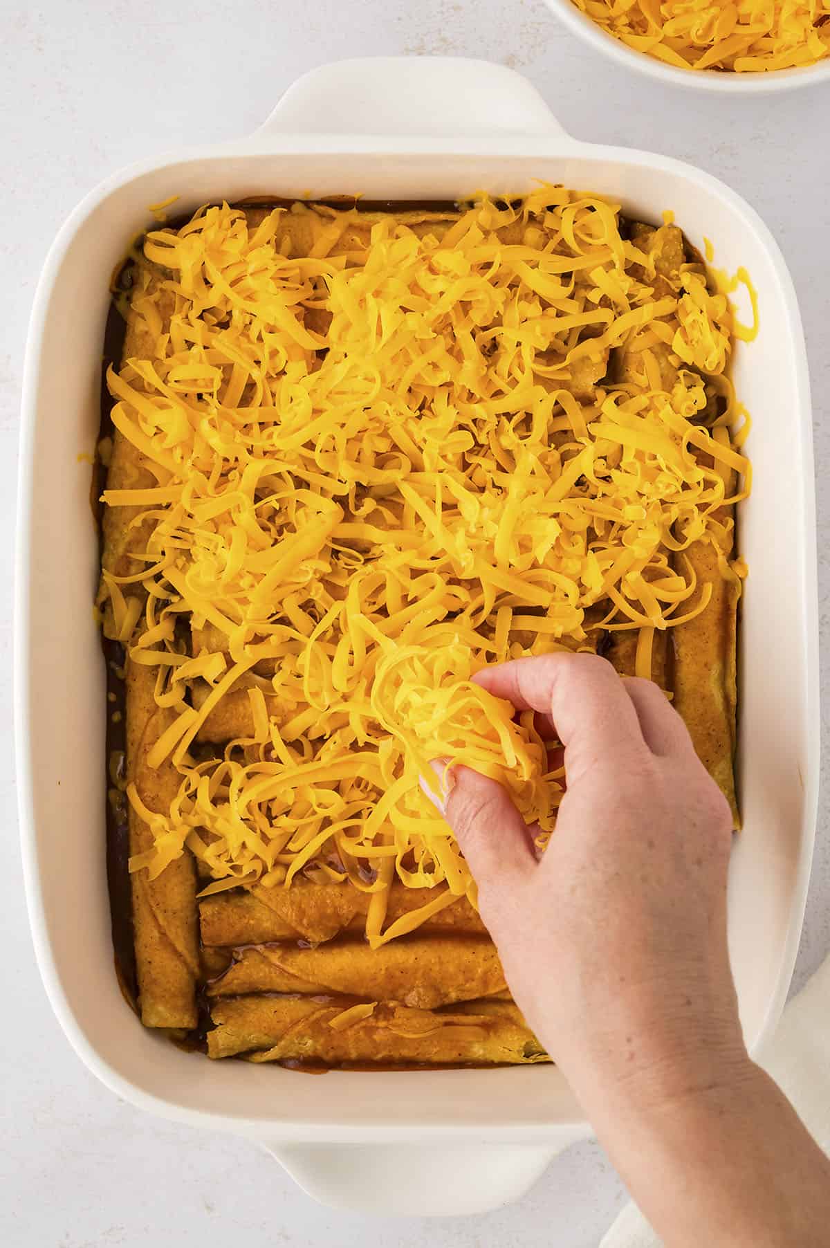 Cheese being sprinkled over taquito enchiladas.