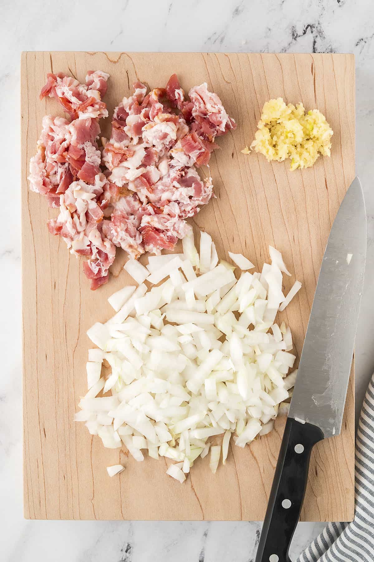 Diced bacon, onion, and garlic on a cutting board.