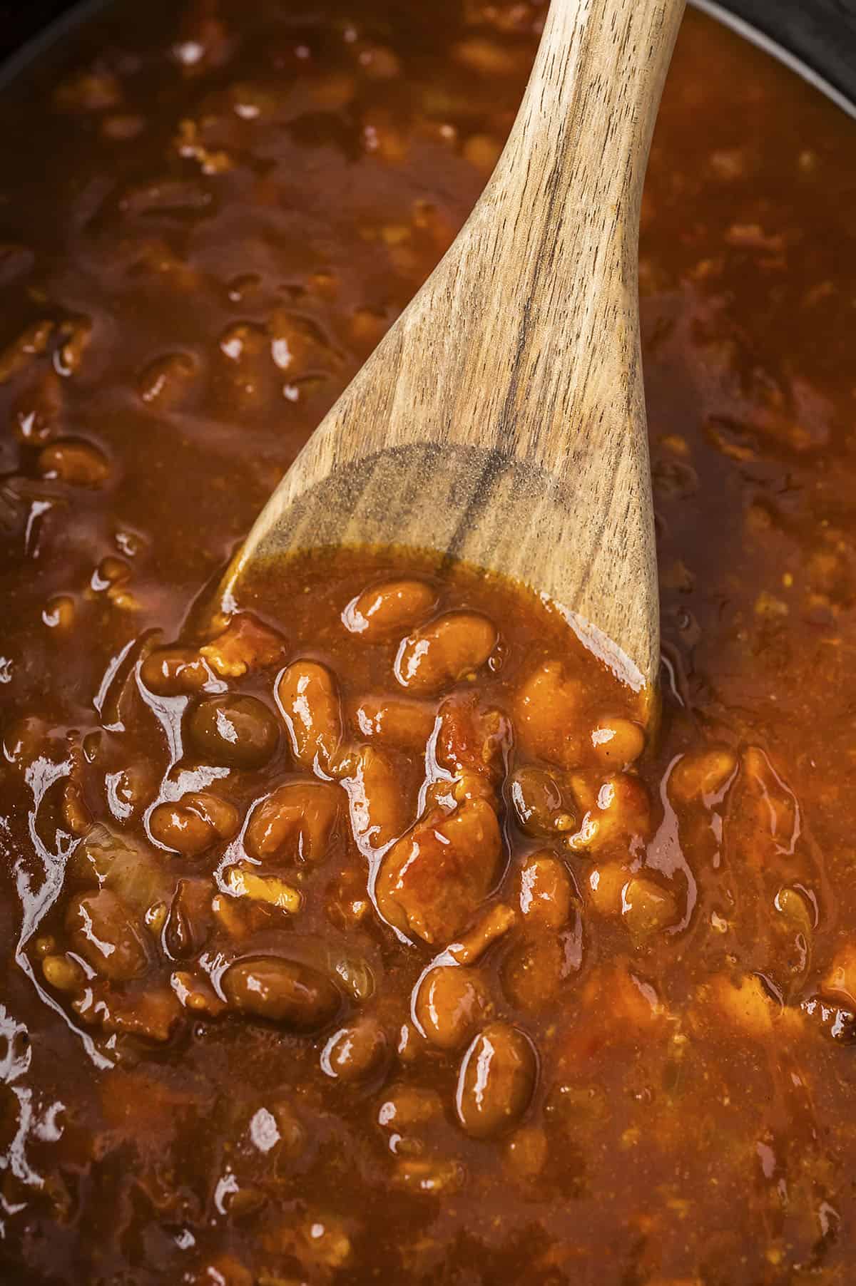 Slow cooker baked beans on wooden spoon.