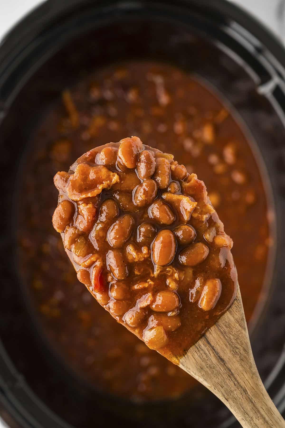 Baked beans on wooden spoon over crockpot.