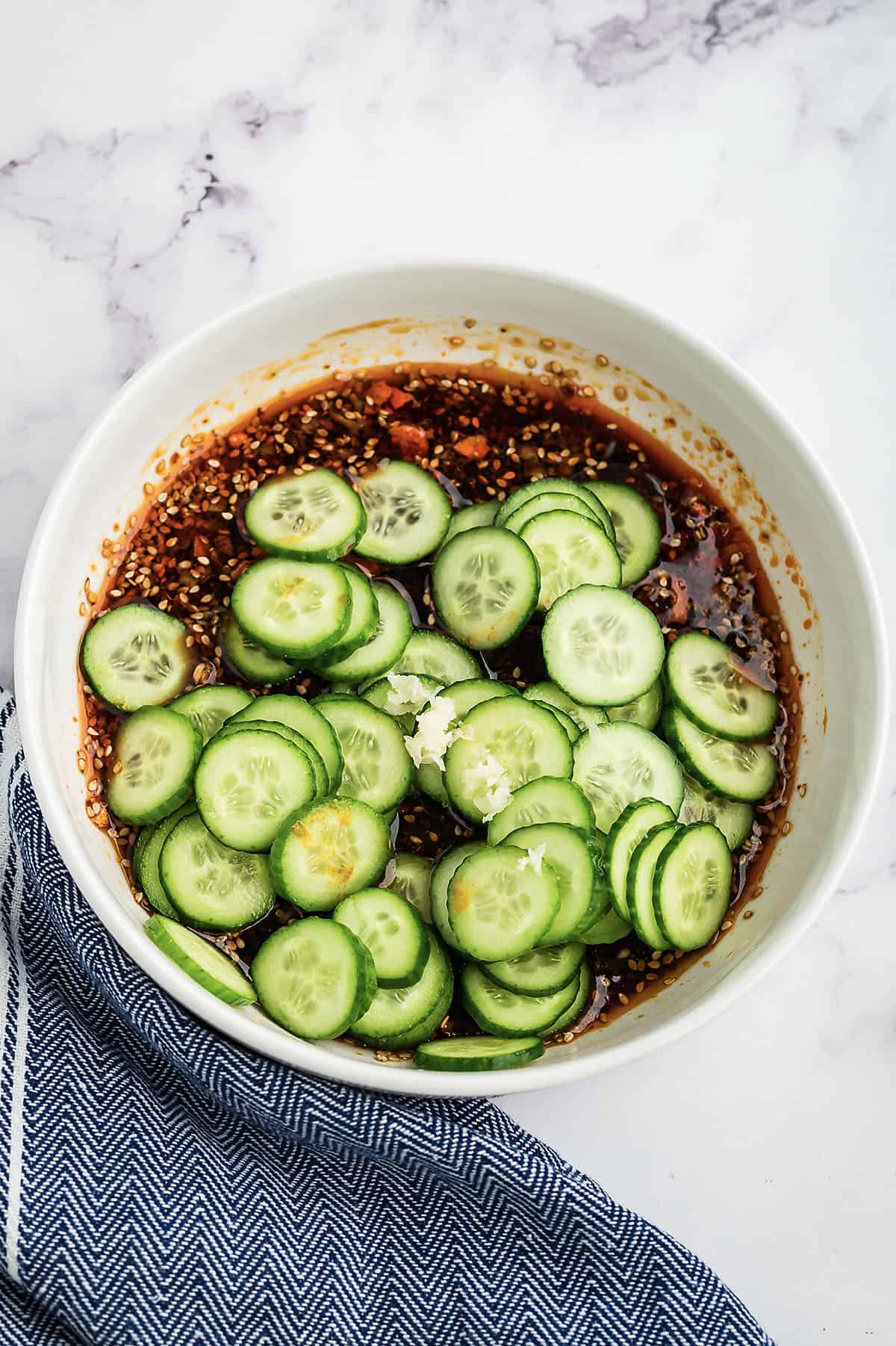 Sliced cucumbers in bowl of dressing.