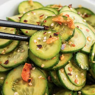 Cucumber salad in white bowl with chopsticks.