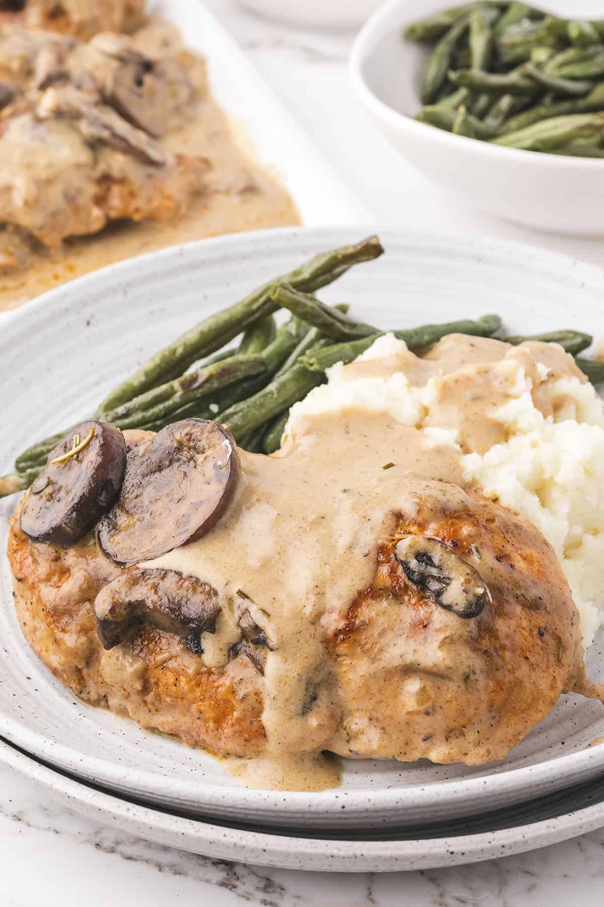 Cream of mushroom chicken on white plate with mashed potatoes and green beans.