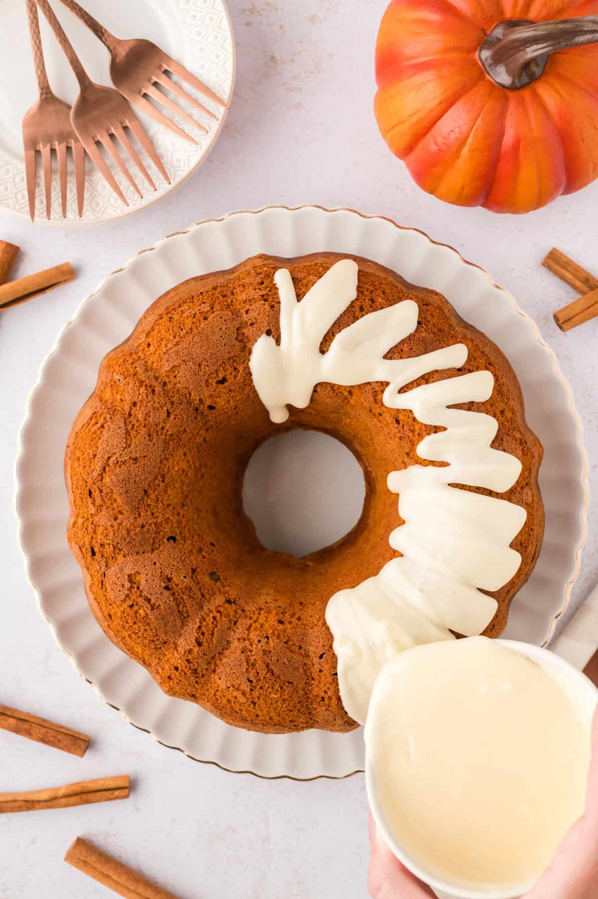 Cream cheese glaze being drizzled over pumpkin bundt cake.