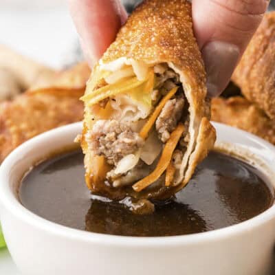 Pork egg roll being dipped in egg roll sauce.