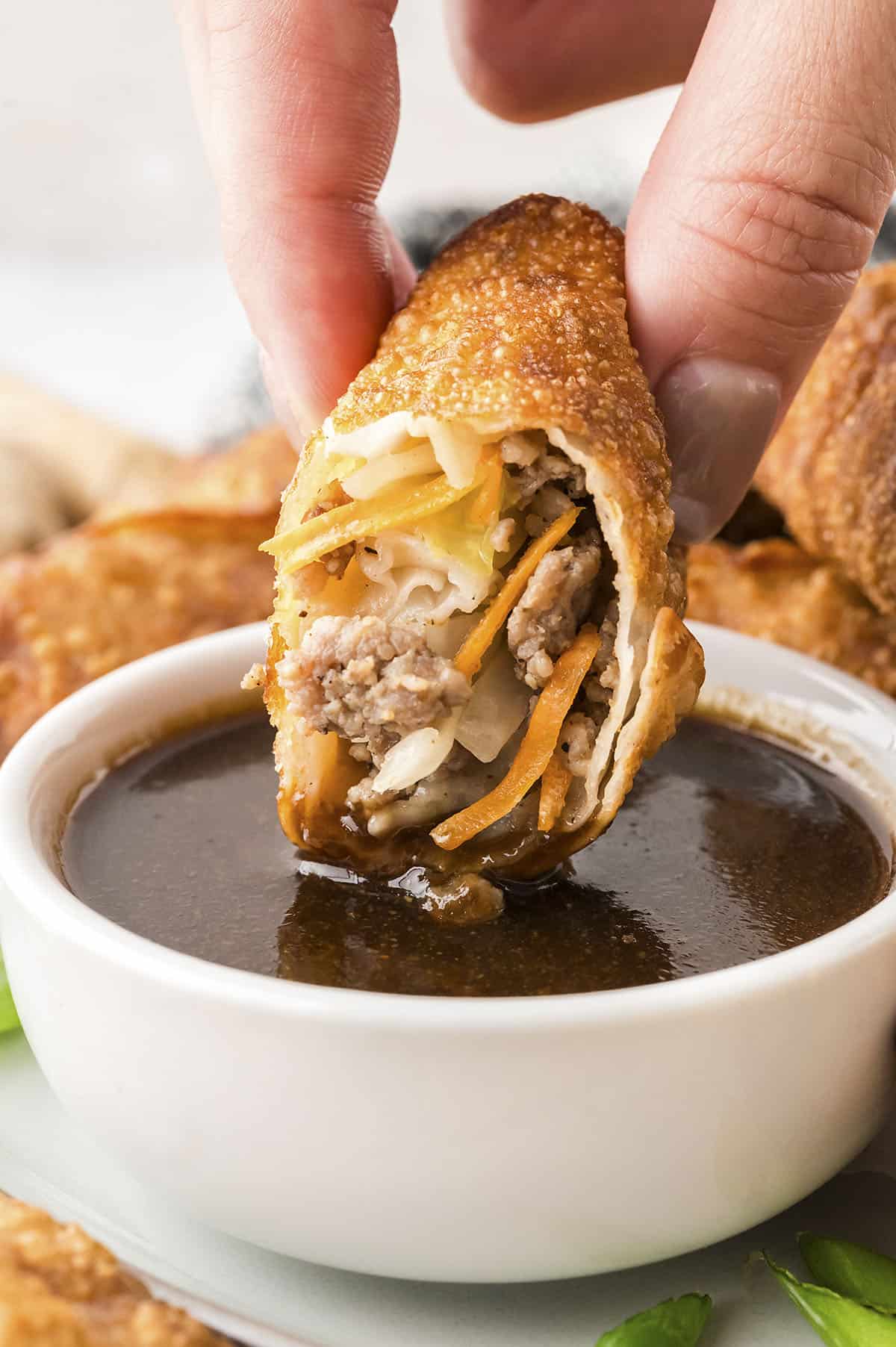 Pork egg roll being dipped in egg roll sauce.