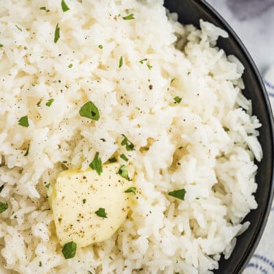 Jasmine rice in a black bowl topped with a pat of butter.