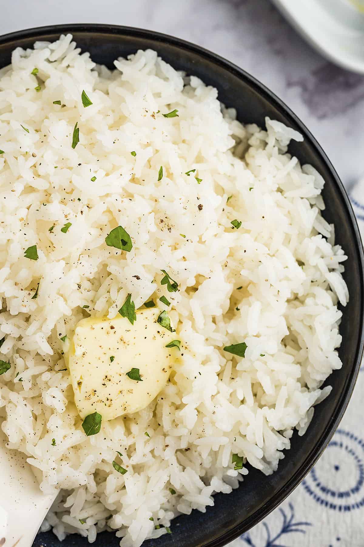 Jasmine rice in a black bowl topped with a pat of butter.