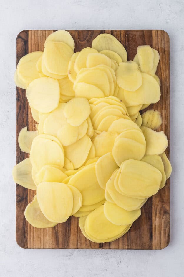 Sliced potatoes on wooden cutting board.