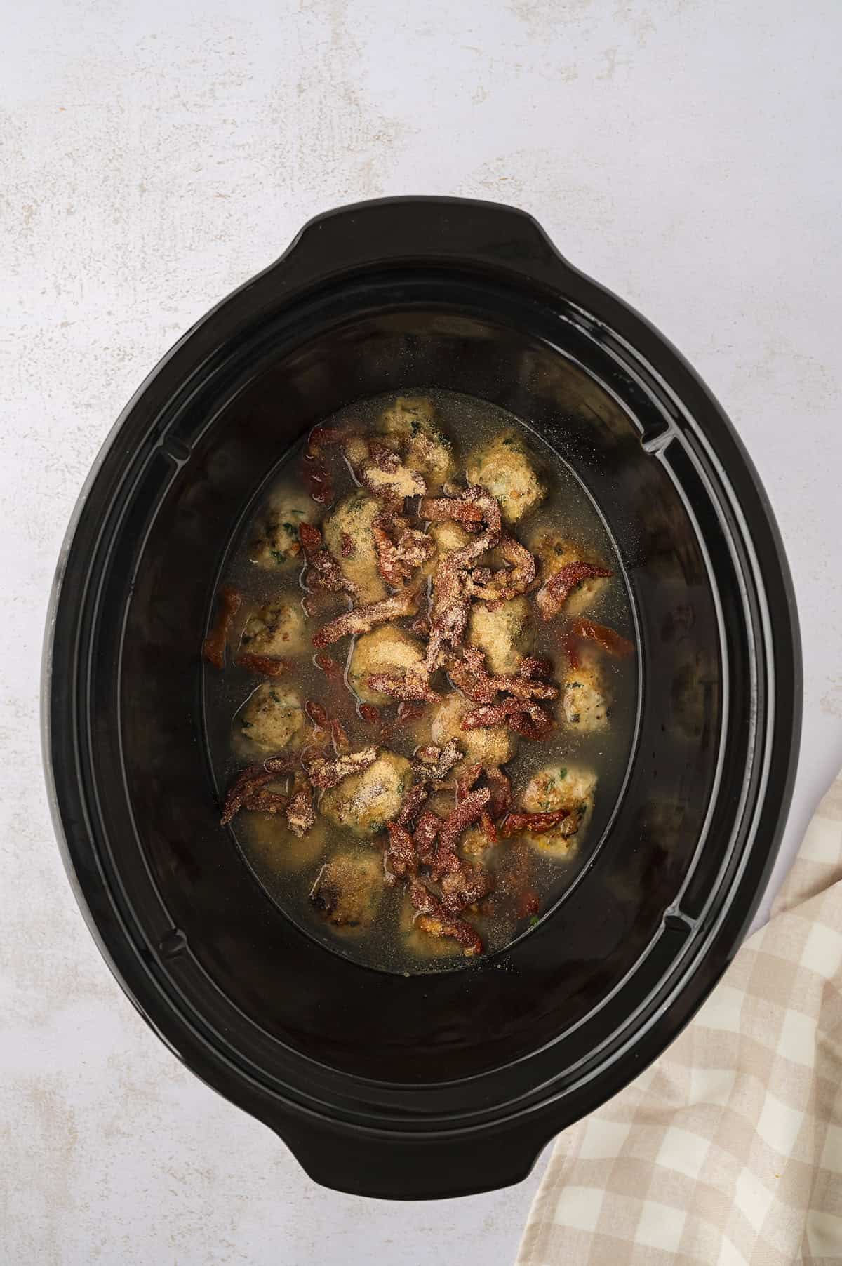 Meatballs, broth, and tomatoes in slow cooker.