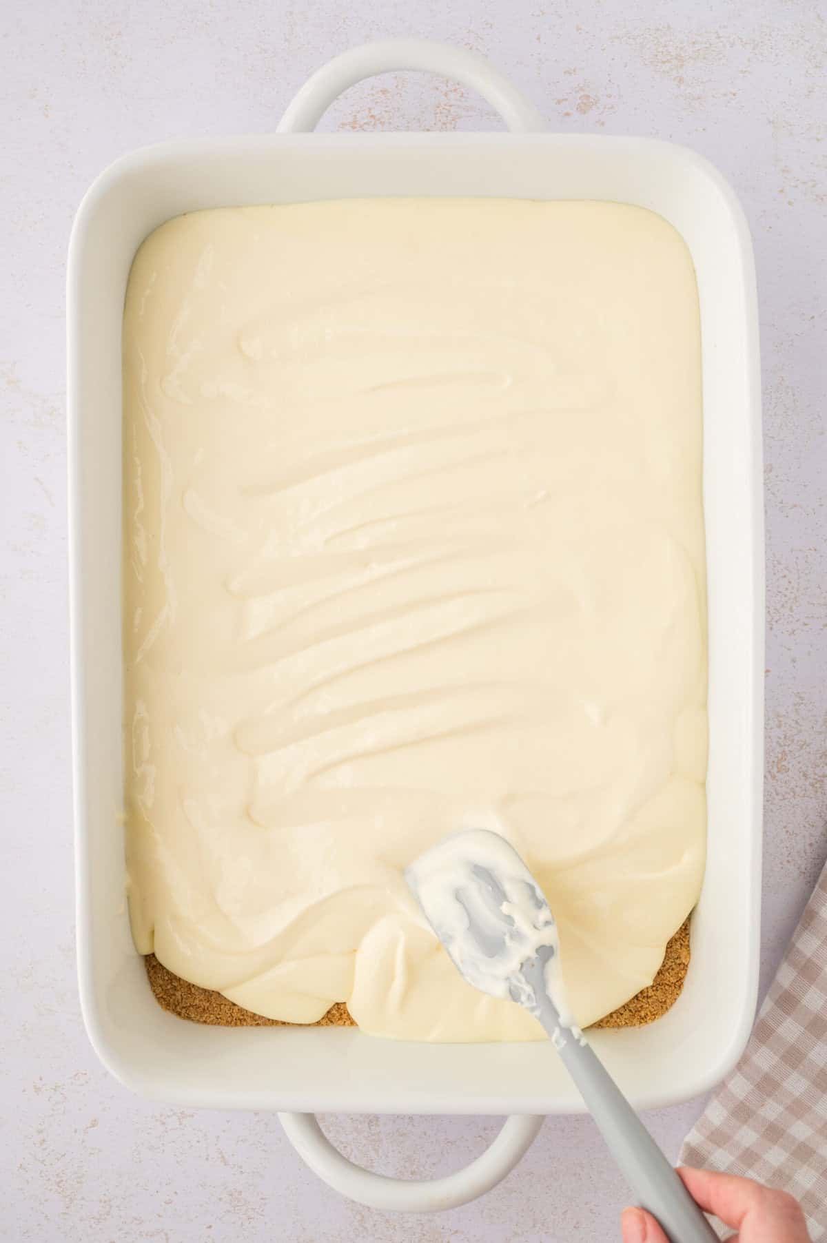 Cheesecake batter being spread over graham cracker crust.