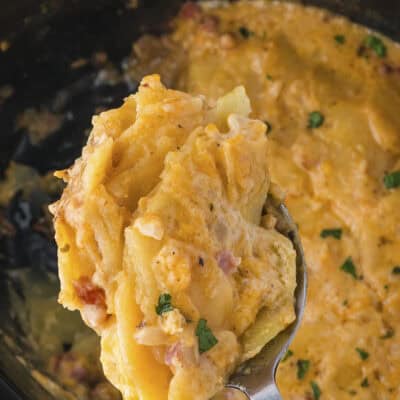 Spoonful of scalloped potatoes with ham over slow cooker.