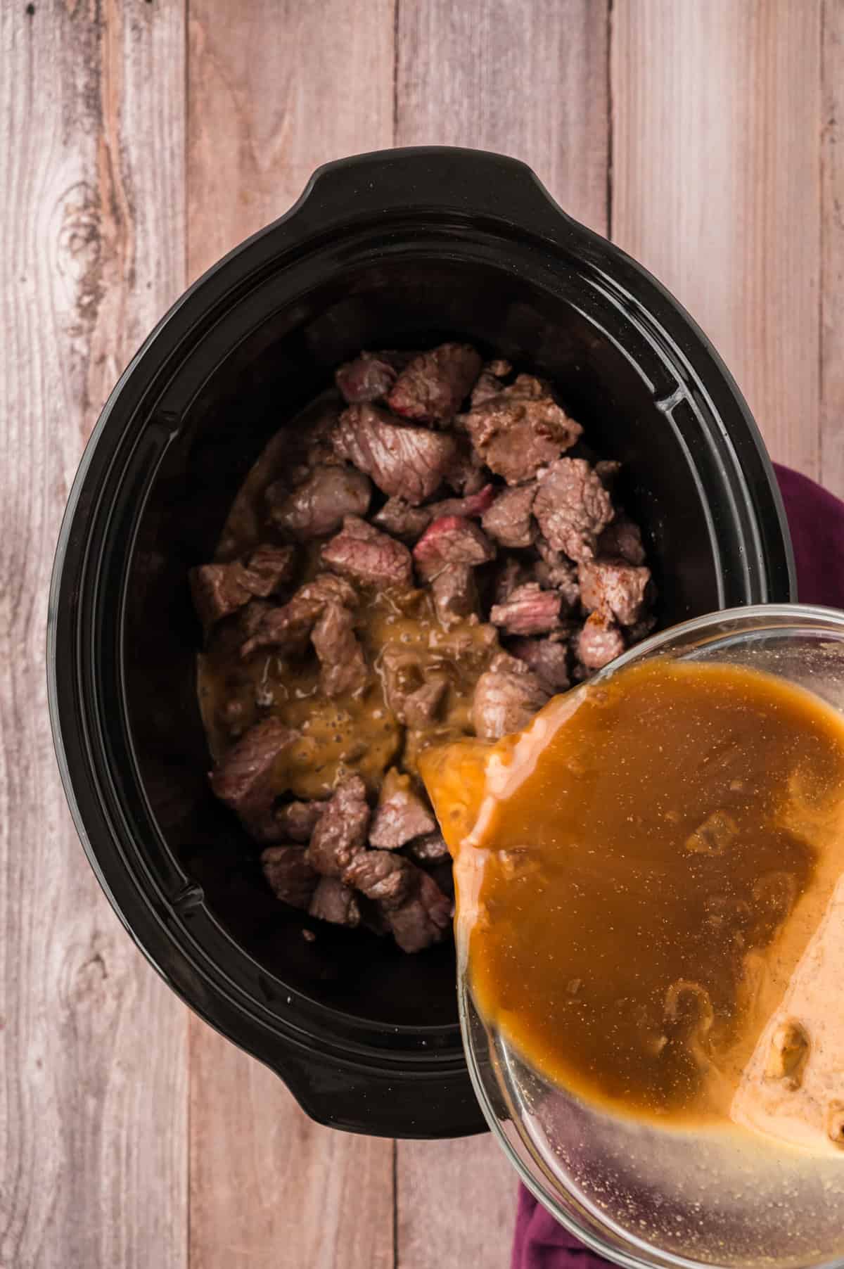 Gravy mix being poured over beef tips in crock pot.