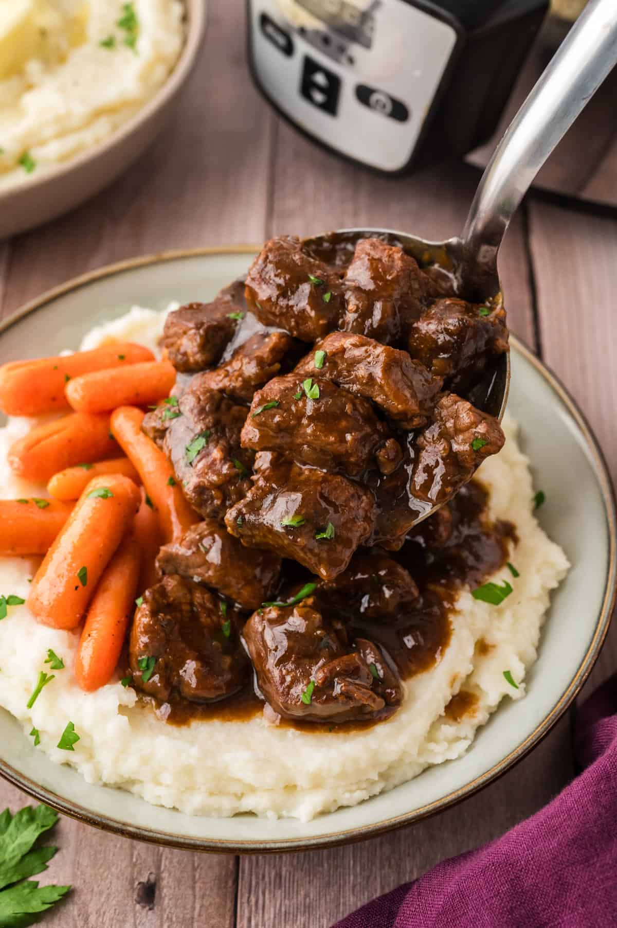 Beef tips being spooned over mashed potatoes.