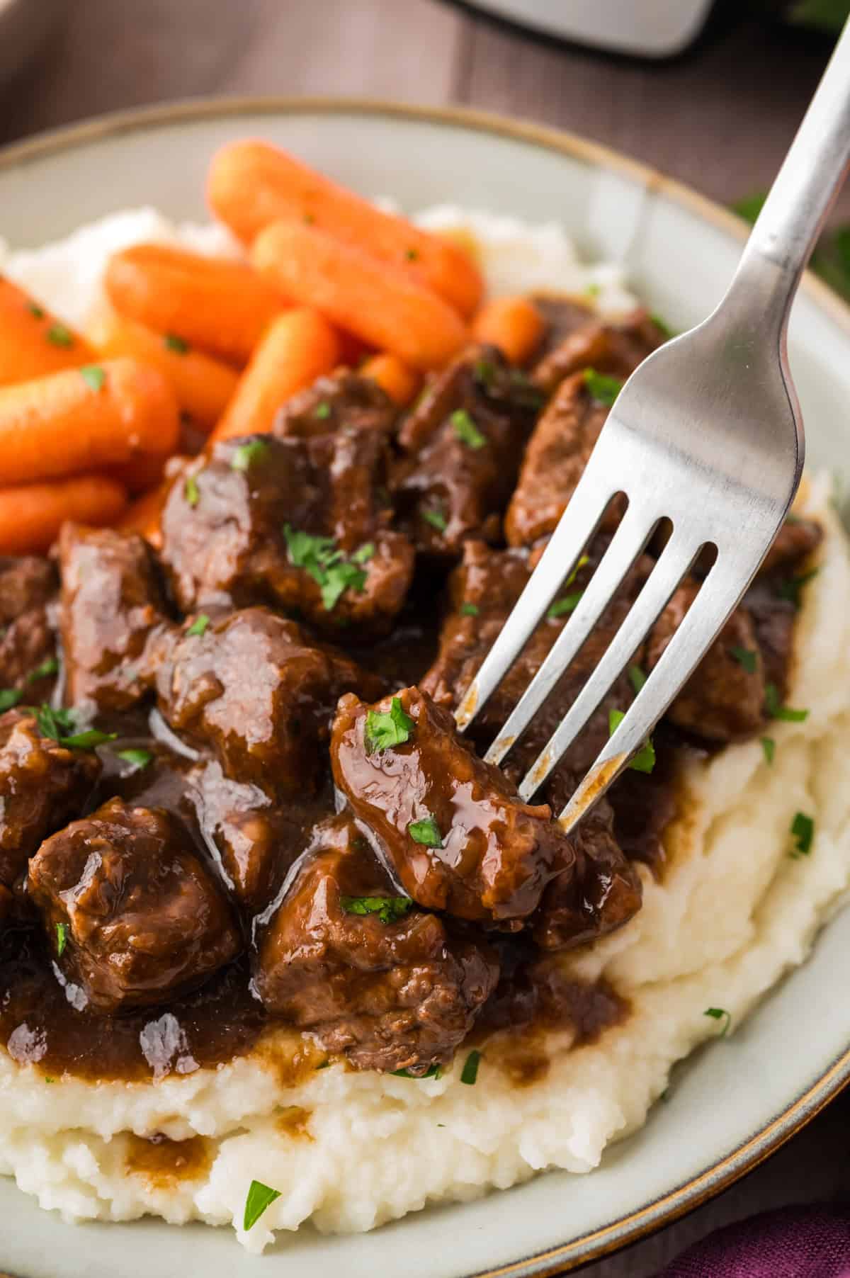 Fork digging into beef tips and gravy over mashed potatoes and carrots.