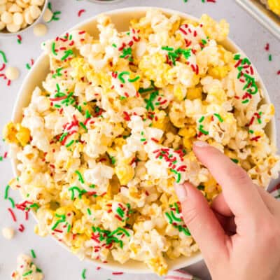 Hand grabbing a bite of Christmas popcorn topped with white chocolate and sprinkles.