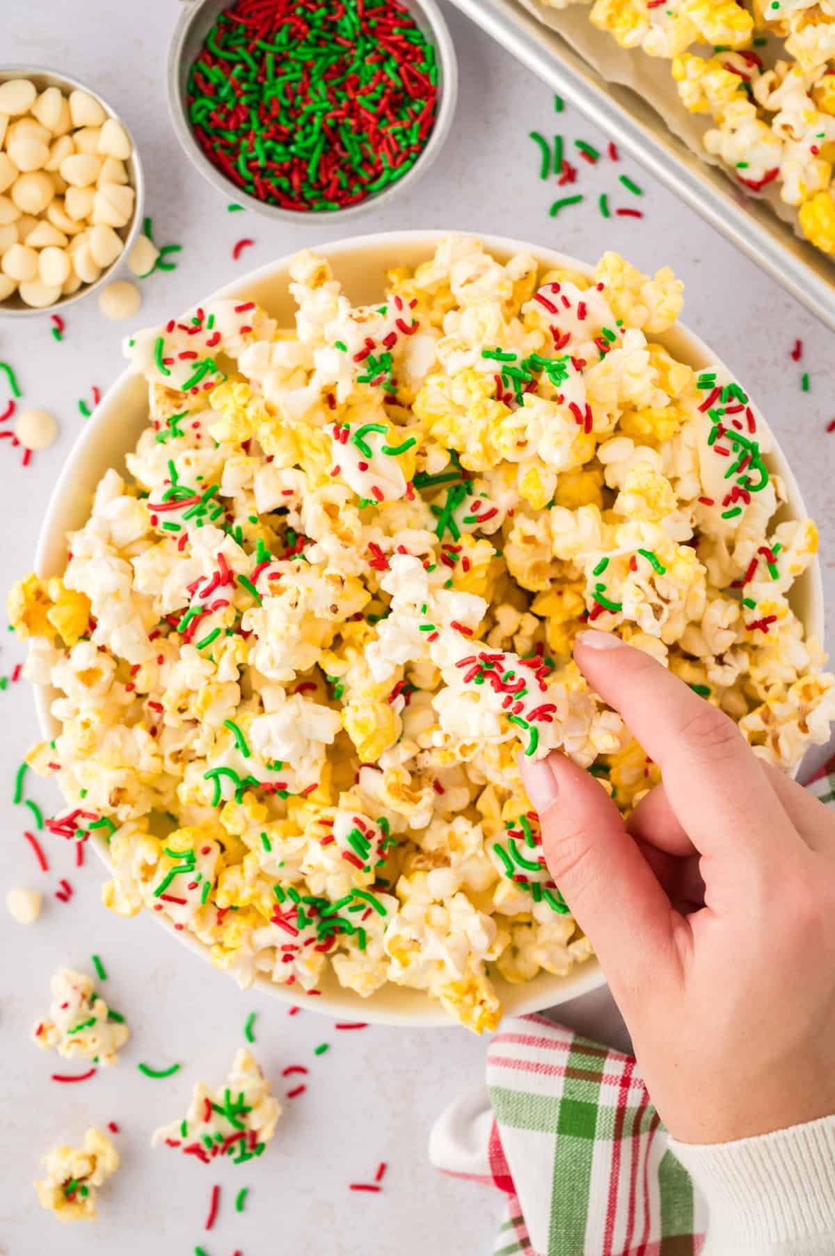 Hand grabbing a bite of Christmas popcorn topped with white chocolate and sprinkles.