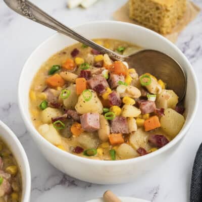 Bowl full of ham and corn chowder with spoon.