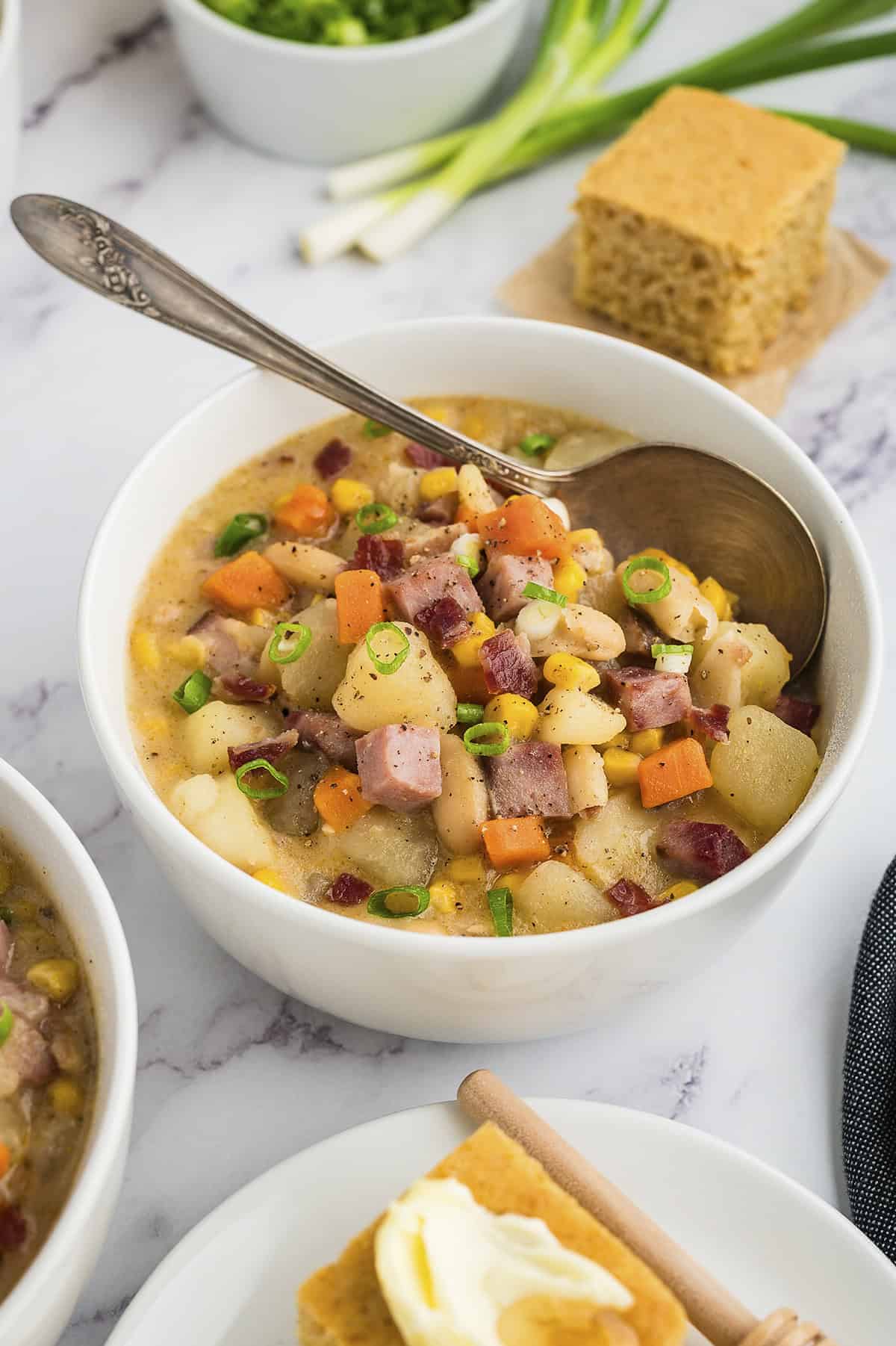 Bowl full of ham and corn chowder with spoon.