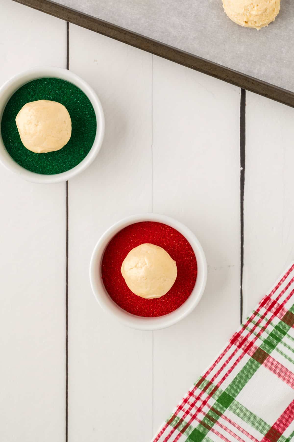 Cookie dough being rolled in red and green sanding sugar.