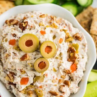 Green olive spread in white bowl surrounded by vegetables and crackers.