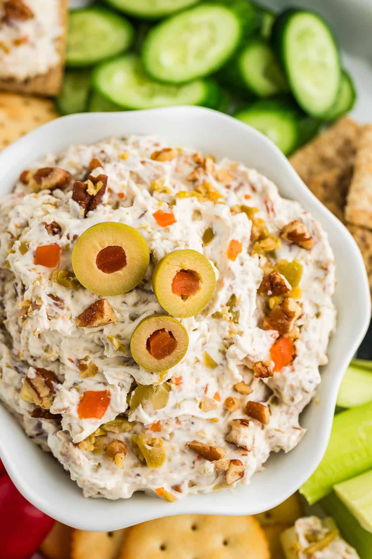 Green olive spread in white bowl surrounded by vegetables and crackers.