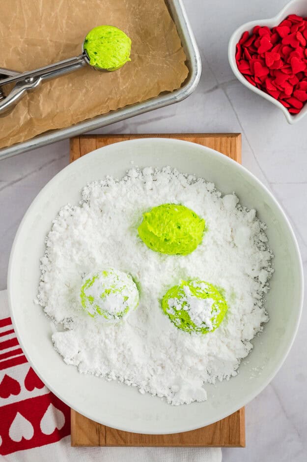 Cookie dough balls being rolled in powdered sugar.