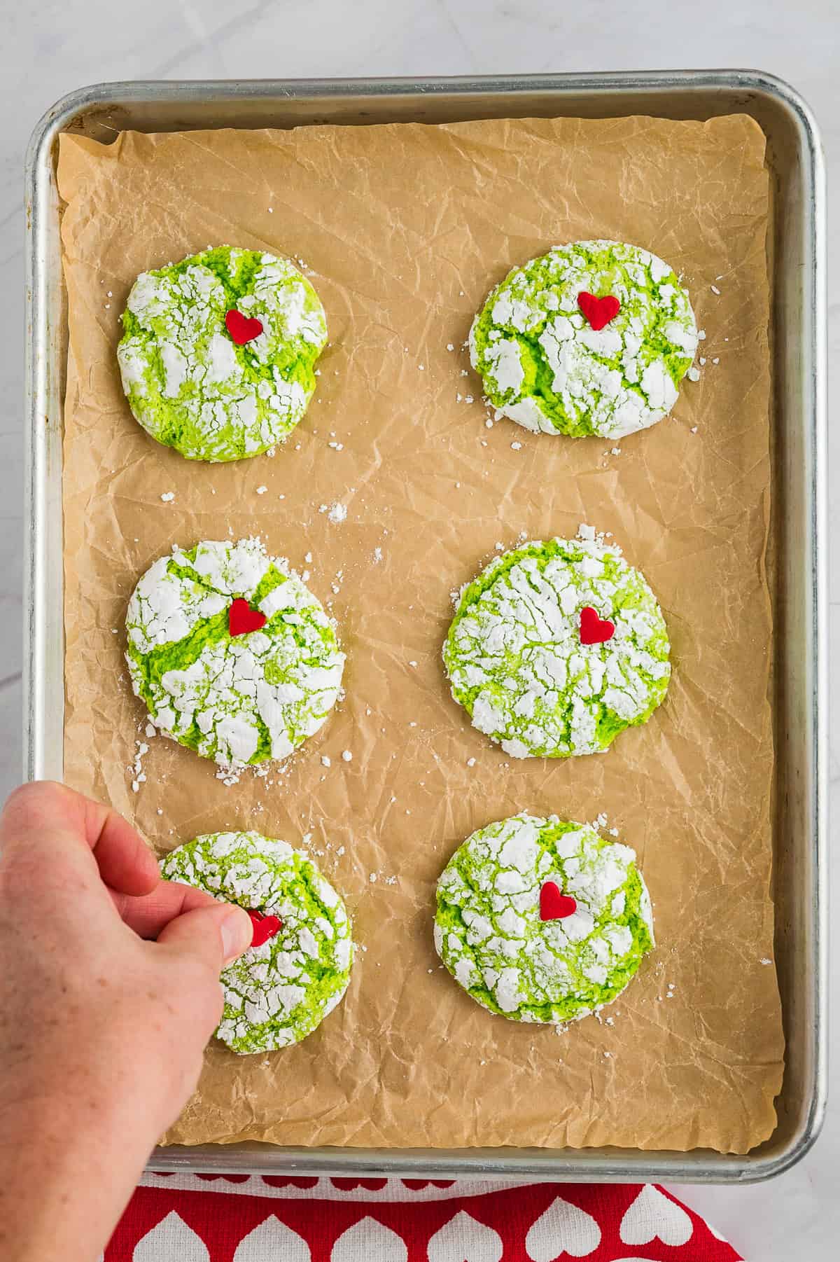 Heart sprinkle being placed on Grinch cookie.