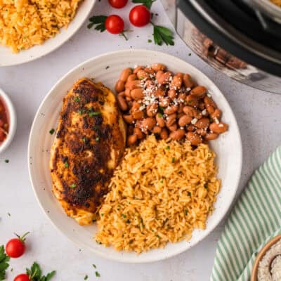 Plate topped with grilled chicken, pinto beans, and Mexican rice.