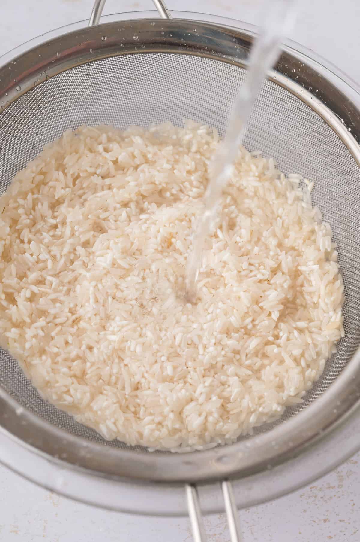 Rice being rinsed in a fine mesh sieve.