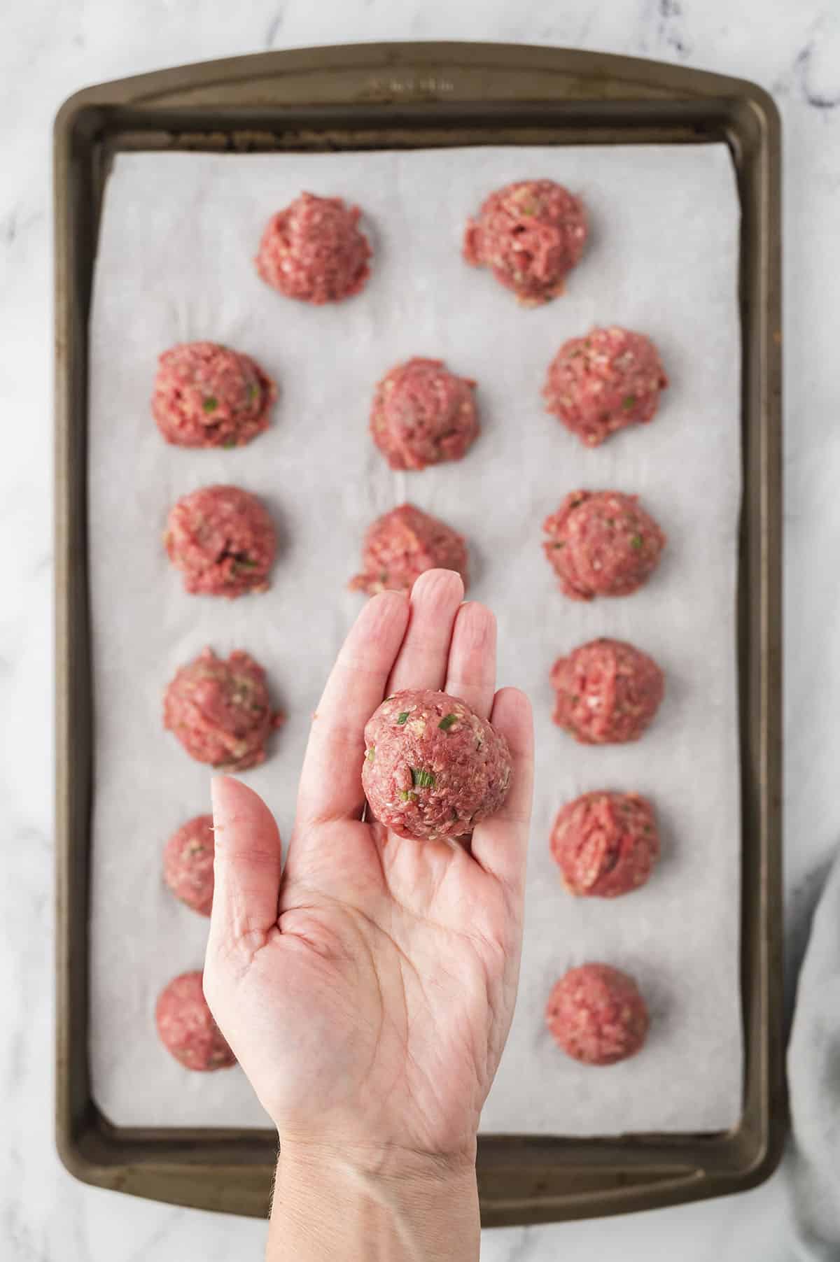 Meatballs being rolled into balls on baking sheet.