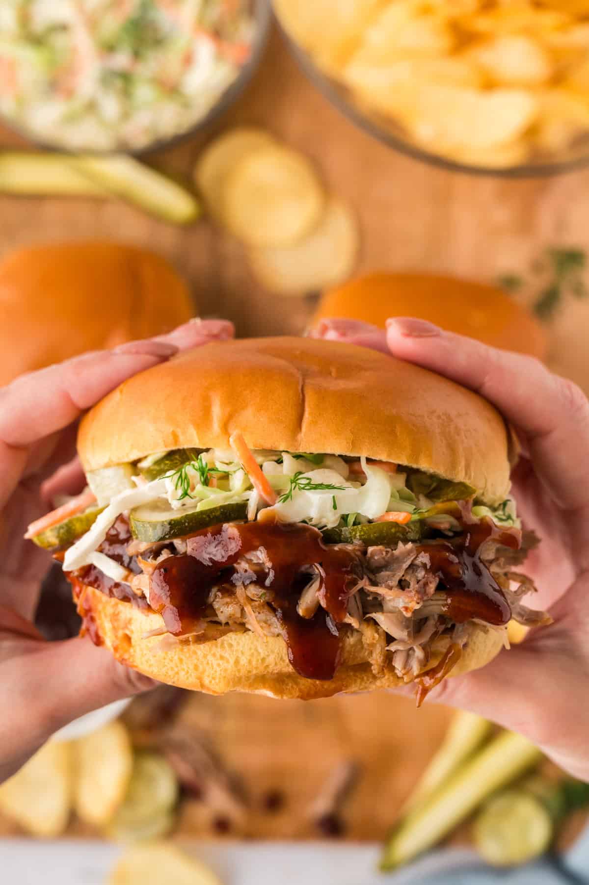 Hands holding a pulled pork sandwich.