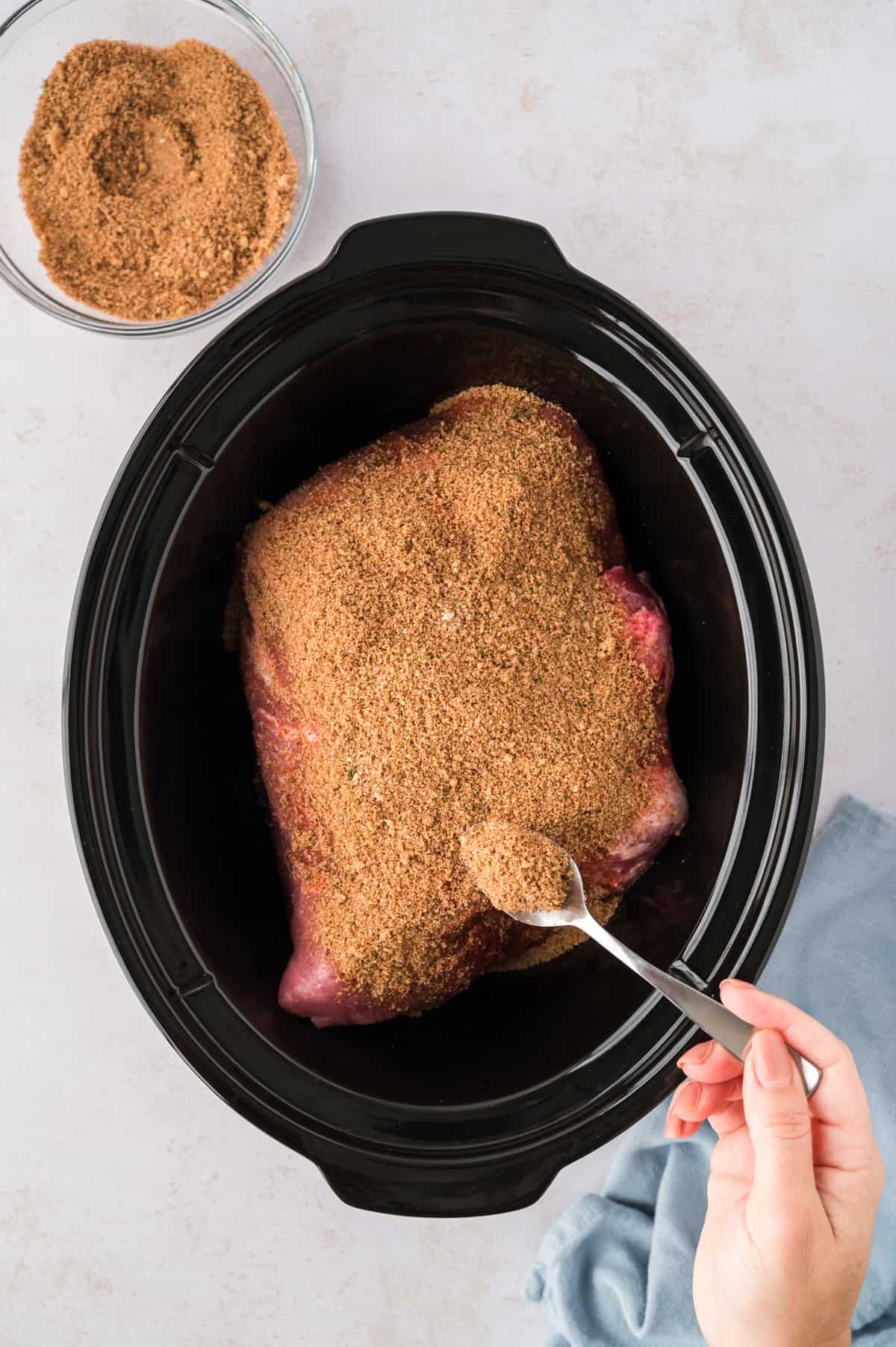 Pork shoulder coated in dry rub in crockpot.