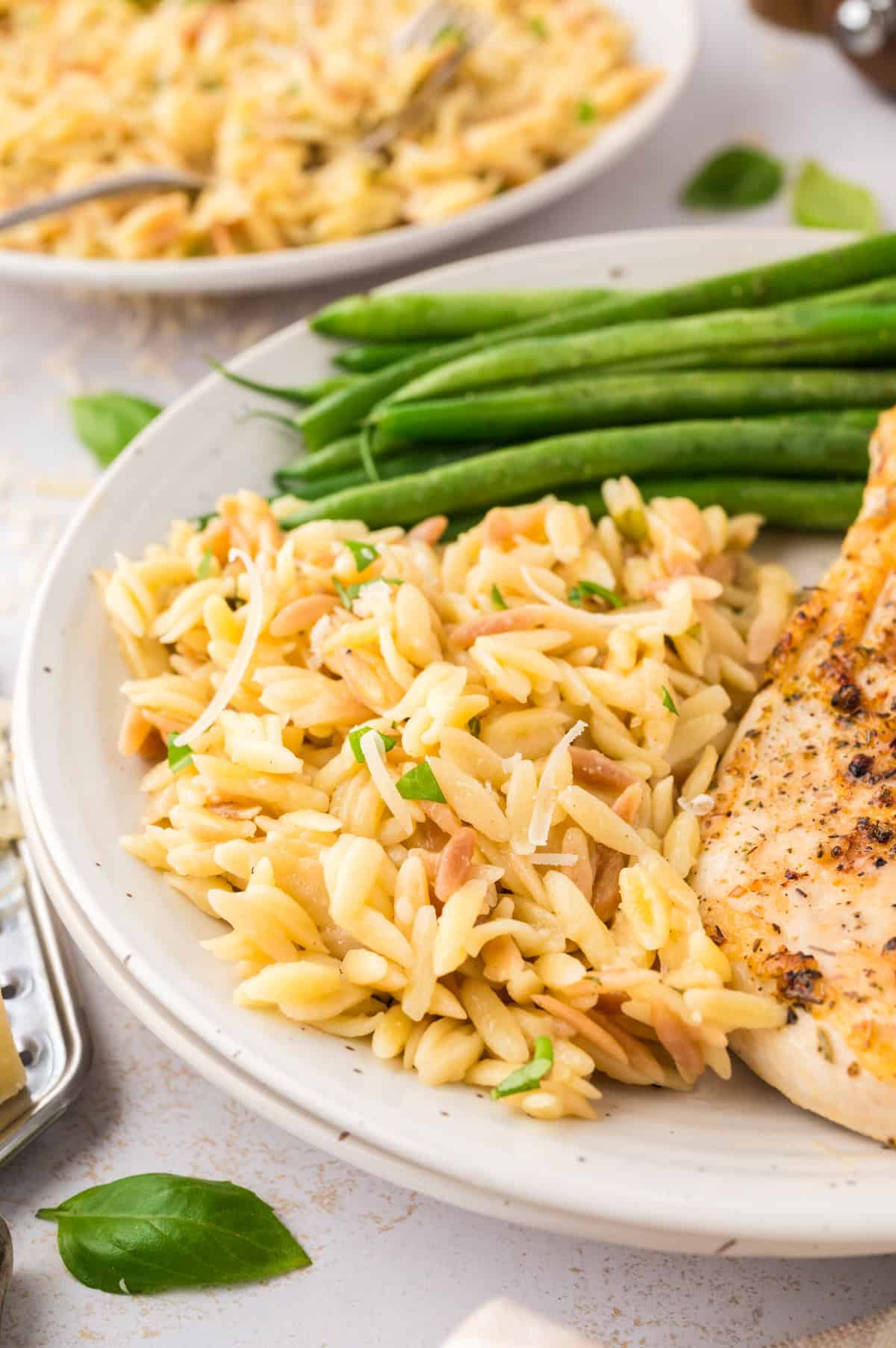 Parmesan orzo on white plate with green beans and chicken.