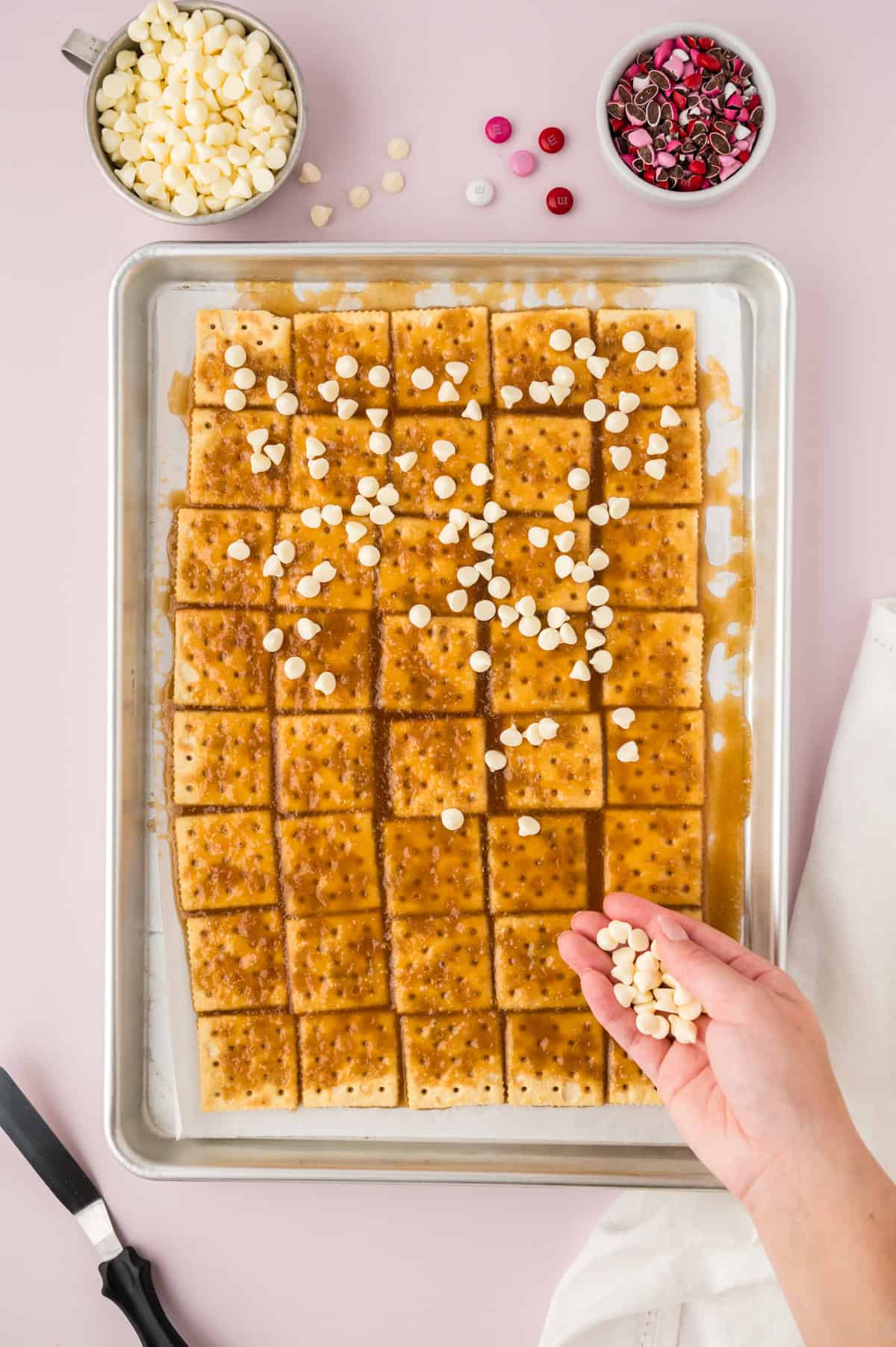 White chocolate chips being sprinkled over crackers.