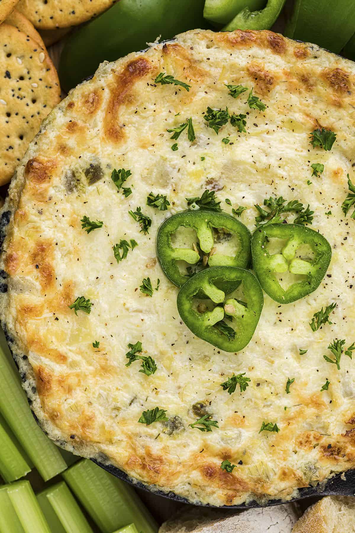 Artichoke jalapeno dip surrounded by crackers and vegetables.